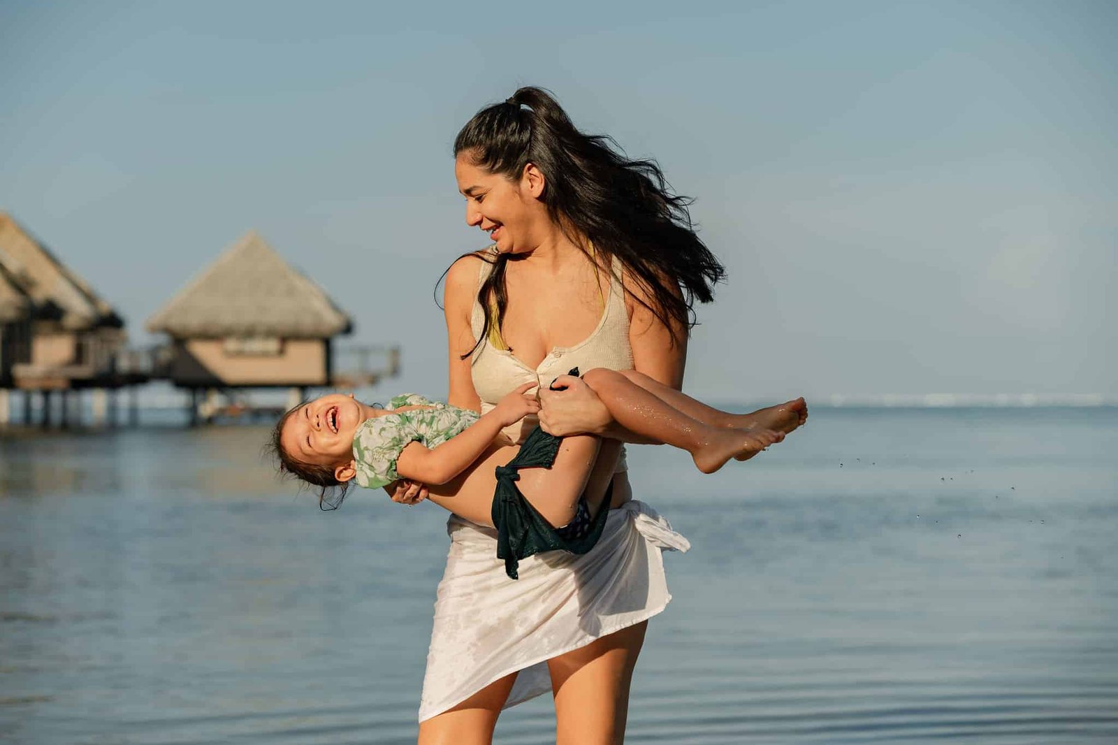 Une mère qui chatouille sa fille tout en la portant sur les bras sur une plage à Tahiti